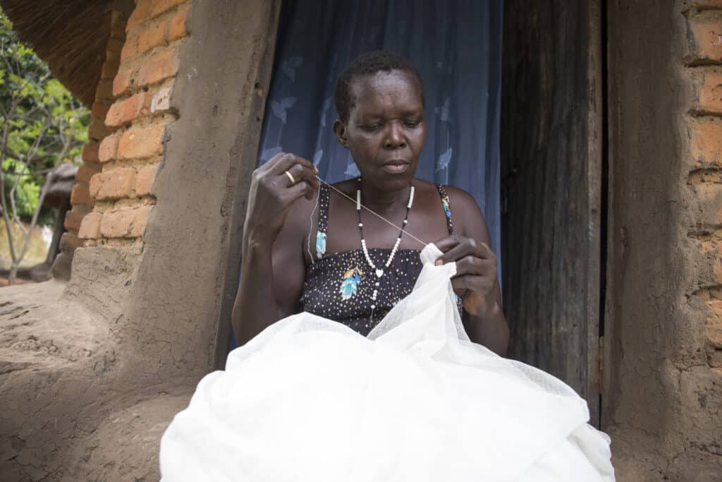 A woman repairs a mosquito net in the West Nile region of Uganda as part of the PMI Uganda Malaria Reduction Activity. (Photo by Jimmy Adriko, for JSI)