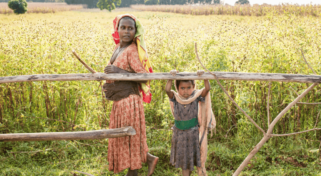 A woman walks with a child behind her in front of a field