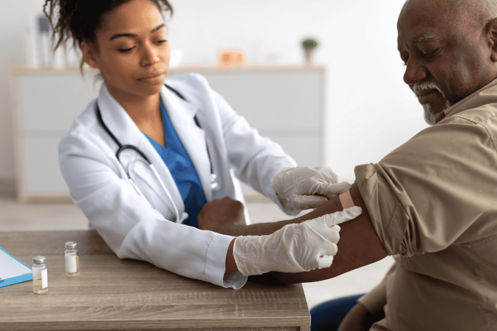 A female healther worker administers a vaccine to an older adult man.