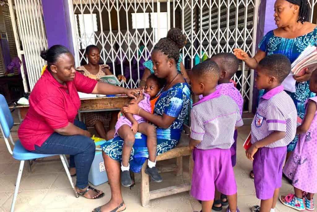 A healthcare worker (left, in red) administering a vaccine to a child at a crèche in Ashaiman, Ghana.