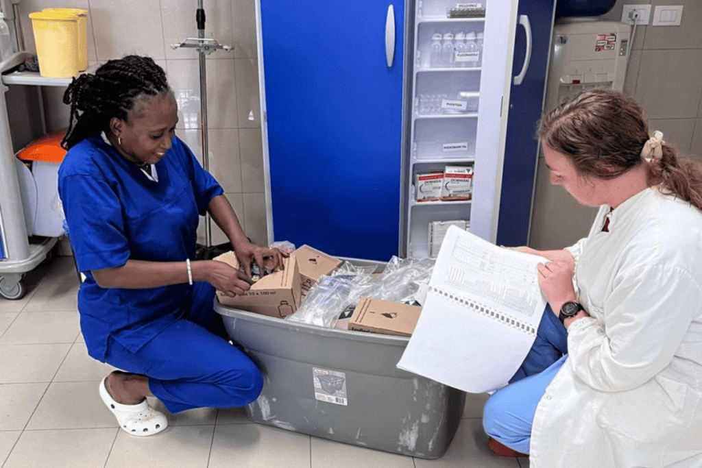 Two female health workers sit on the floor going through a container of medicines.