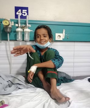 A young girl smiles from a hospital bed.