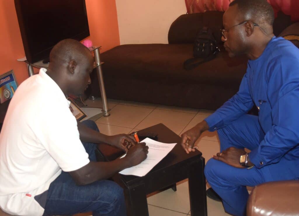 Community leader Michael Nyam Sila (left) filling out documents after a community engagement on HPV with a HAPPI staff member.